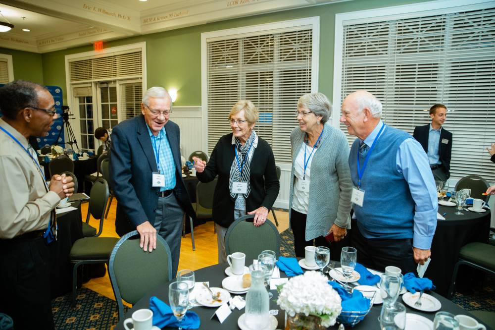 Five alumni stand together and talk to one another at the Reunion Dinner.